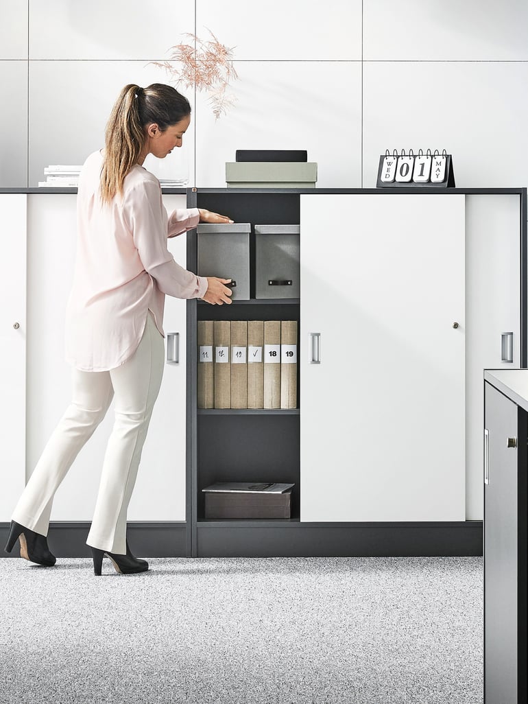 A girl is retrieving a storage box from a cabinet with sliding doors.