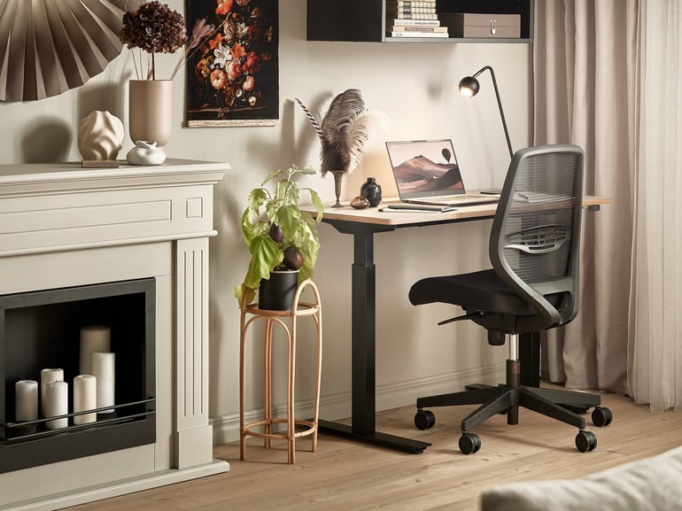 An organised home office space in muted colours. The working area consist on a standing desk, ergonomic offic chair, laptop and desk lamp