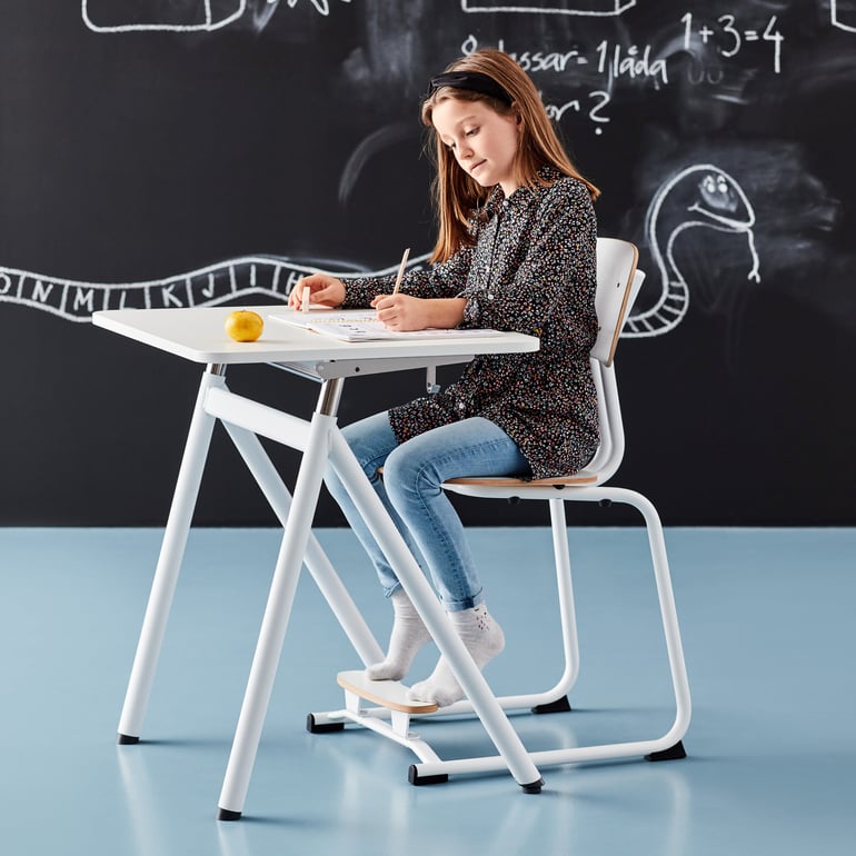 a girl sitting at a school desk writing on a notebook