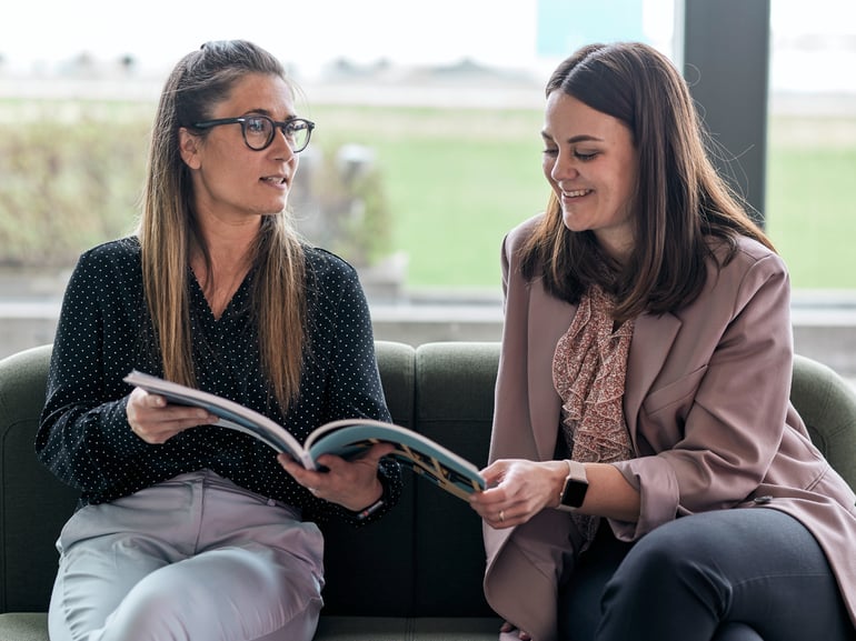 Two people sitting next to each other and looking in a newspaper