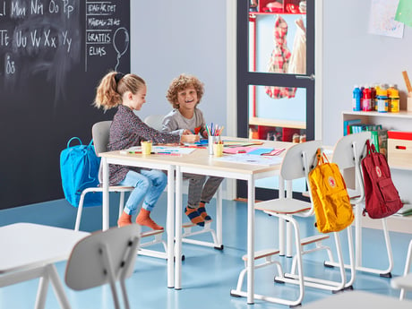 To børn sidder ved skoleborde i et klasselokale
