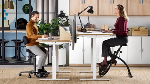 Two people sitting at sit-stand desks