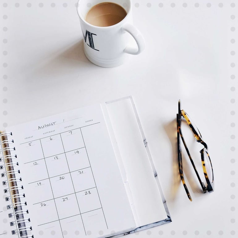 En tom kalender på et skrivebord med et par briller og en kop kaffe ved siden af