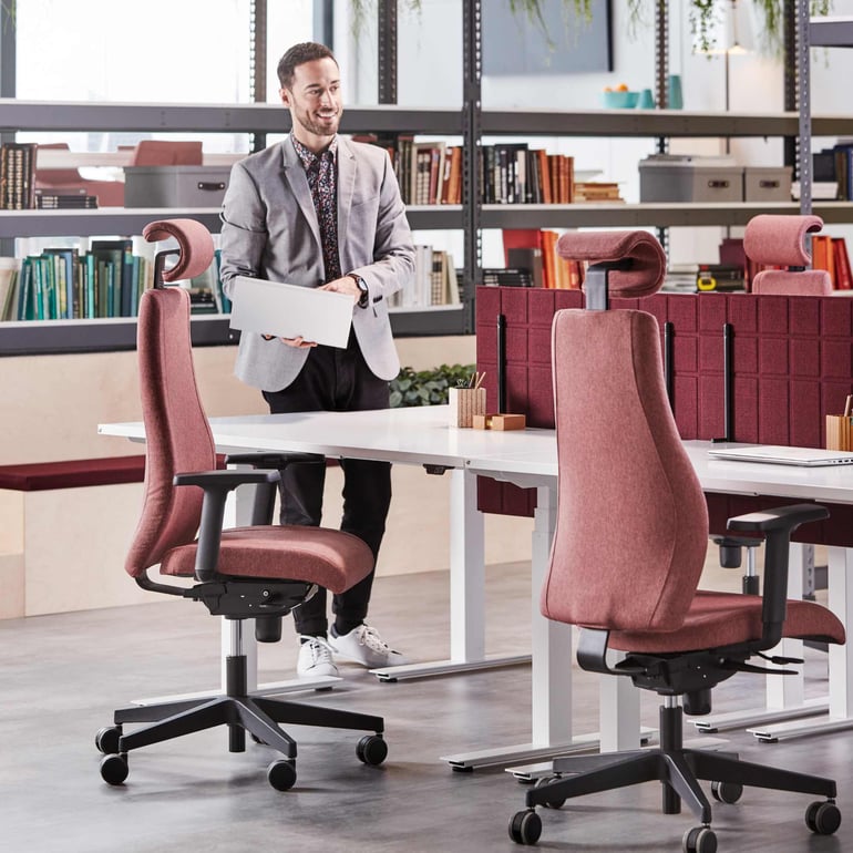 En mand iført blazer står i et kontor med bordeaux kontorstole og bordskærme