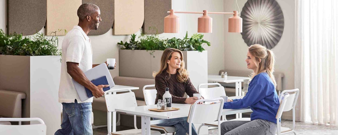Tre kolleger holder en kort kaffepause i kantinen på deres arbejdsplads