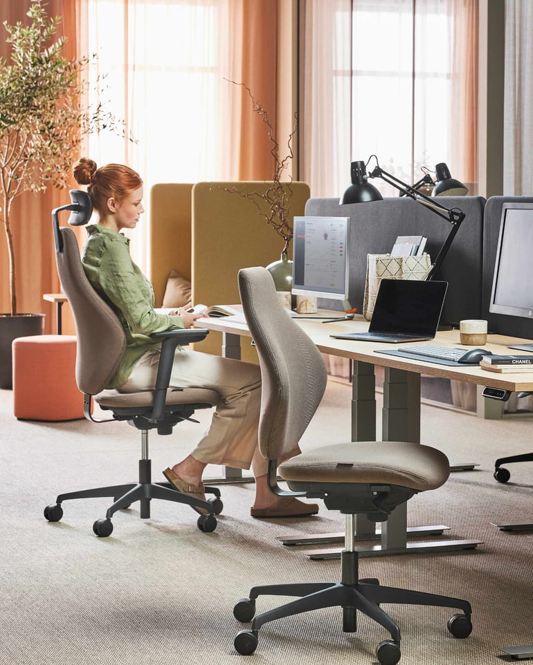 En kvinde sidder på en kontorstol ved et skrivebord og kigger ind i sin computerskærm