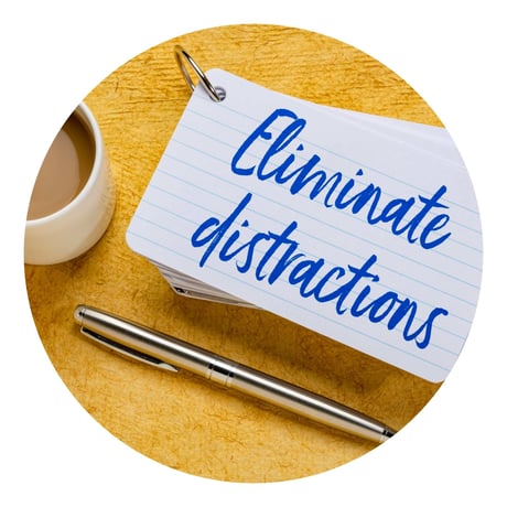 En seddel hvor der står "eleminate distractions" ligger ved siden af en kuglepen og en kop kaffe