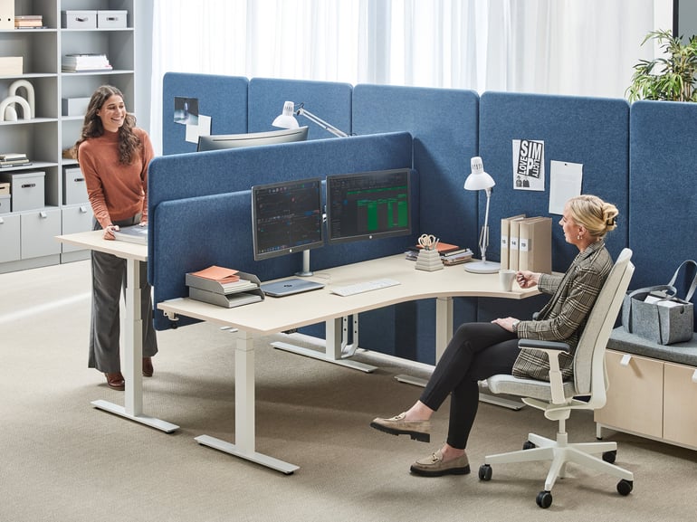 To kollegaer på et kontor med bordskærme og skærmvægge