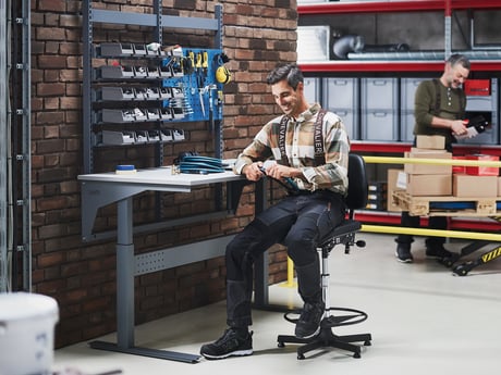 En mand sidder på et lager og arbejder ved et værkstedsbord