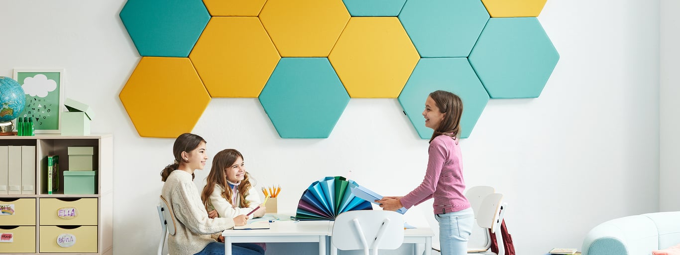 Sekskantede akustikpaneler i gul og blå på væggen i et klasselokale  