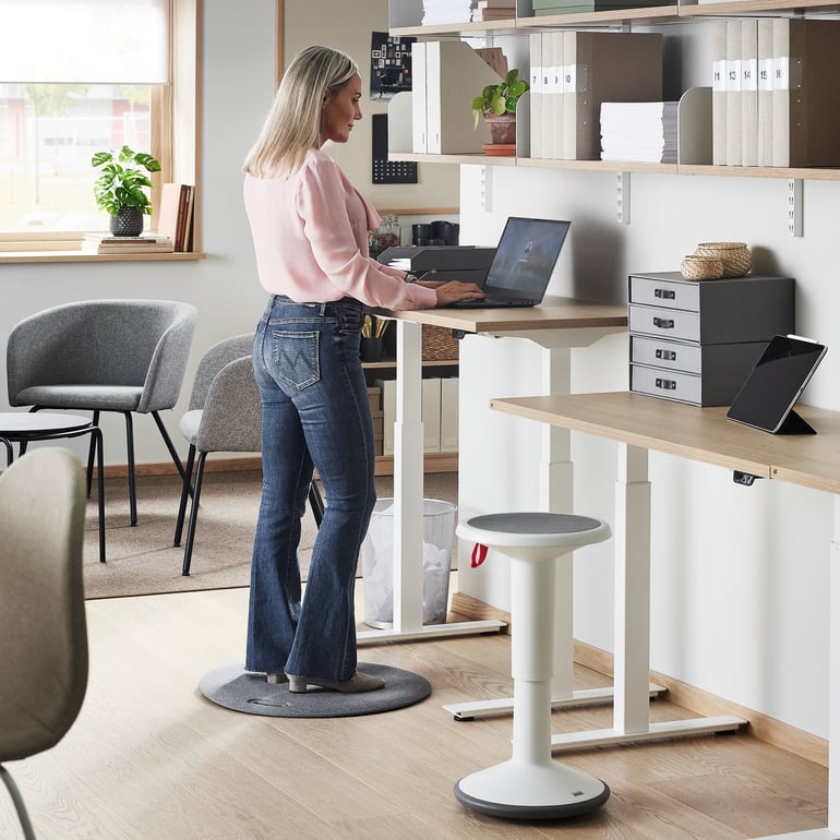 Woman standing to work at a sit-stand desk in an office 