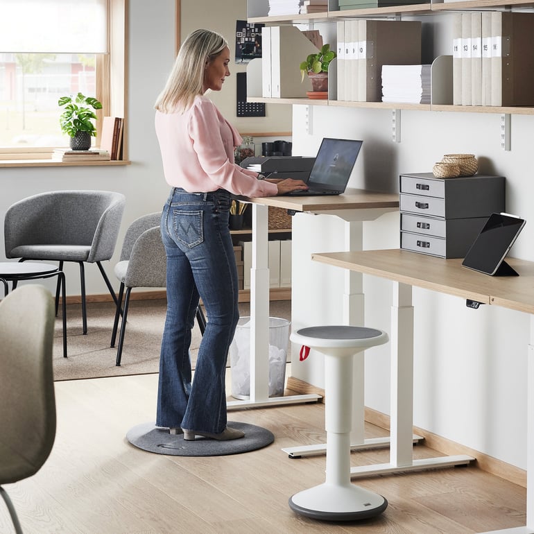 Woman standing to work at a sit-stand desk in an office