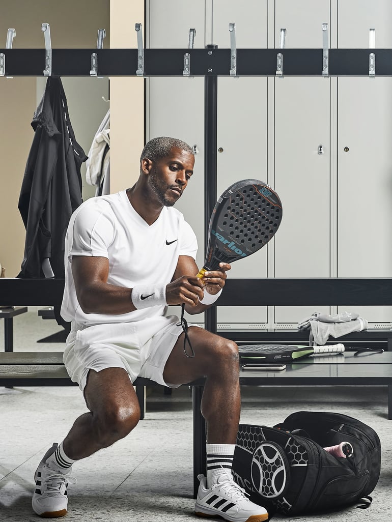 Ein Mann hält sein Tennischschläger und sitzt auf einer Bank in der Umkleidekabine