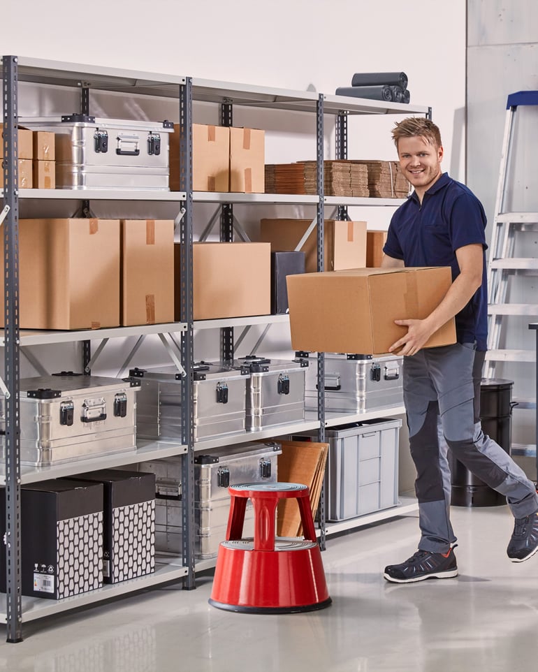 Man in a warehouse with shelves carries a storage box