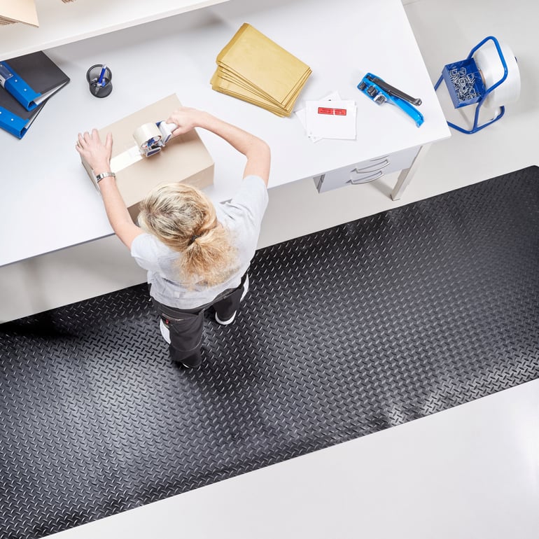 Woman standing on a workplace mat at a packing station packing a box
