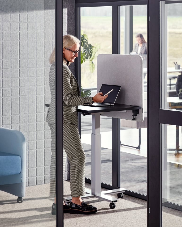 A woman is standing at a height-adjustable desk in a room equipped with sound absorbers