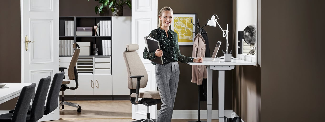 Žena v kanceláři stojí u výškově nastavitelného stolu