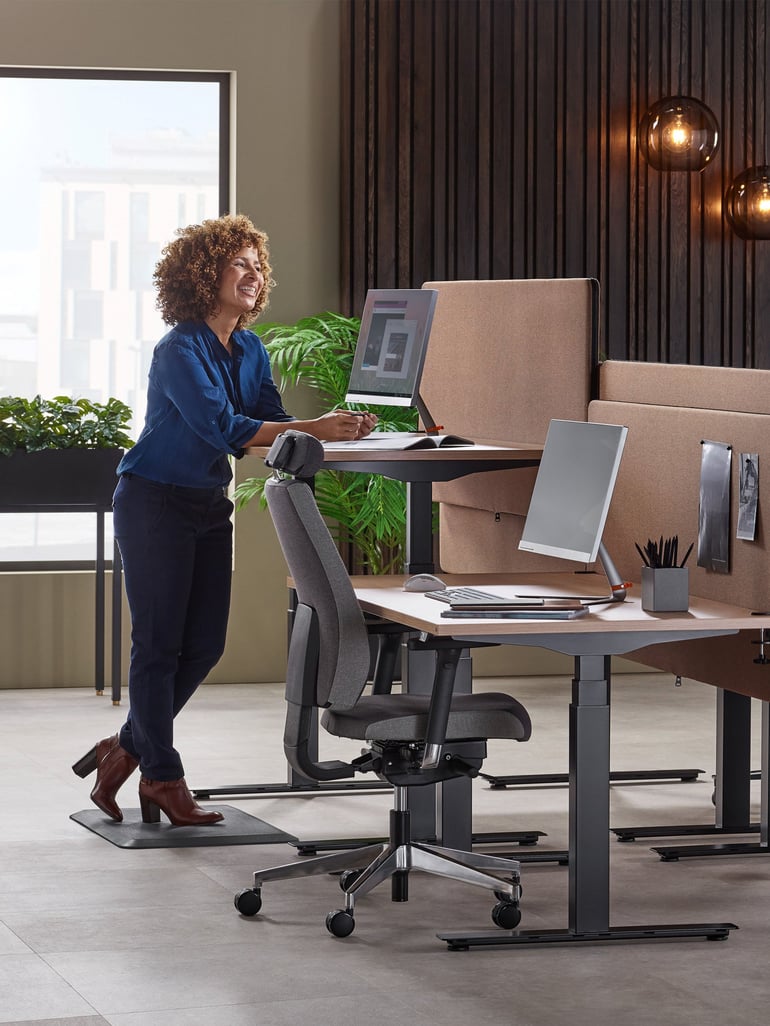 En kvinna står på en arbetsplatsmatta vid ett höj- och sänkbart skrivbord