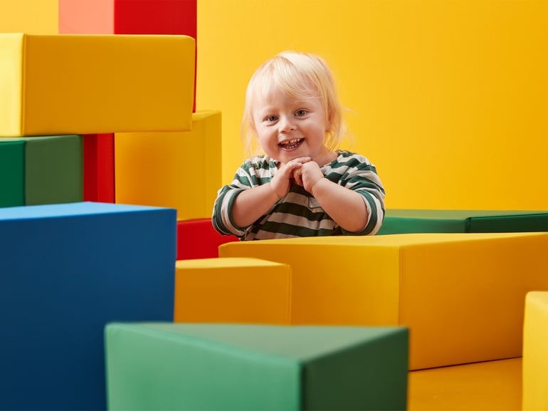 Et barn kigger frem bag en masse farvestrålende skumpuder