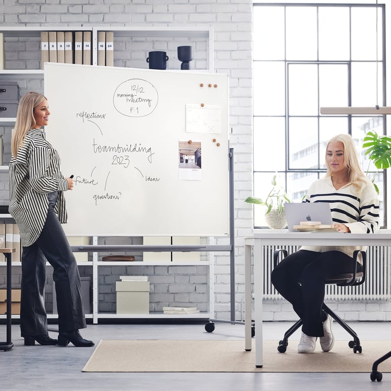 To kvinder brainstormer ved et whiteboard på et lyst kontor