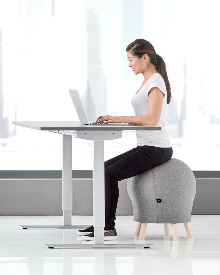 Kvinna sitter på balanspall vid ett höj- och sänkbart skrivbord