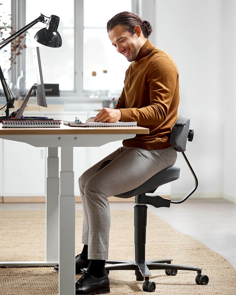Leende man sitter på en balanspall vid sin arbetsplats