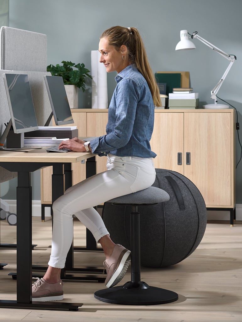 Eine Frau sitzt auf einem Sitzball und arbeitet an ihrem Schreibtisch