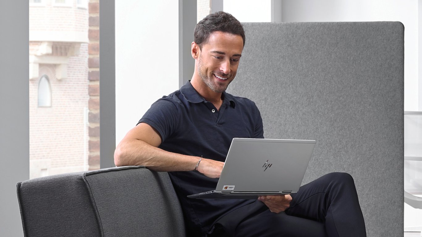 Smaidošs vīrietis šēž dīvānā un skatās laptopā