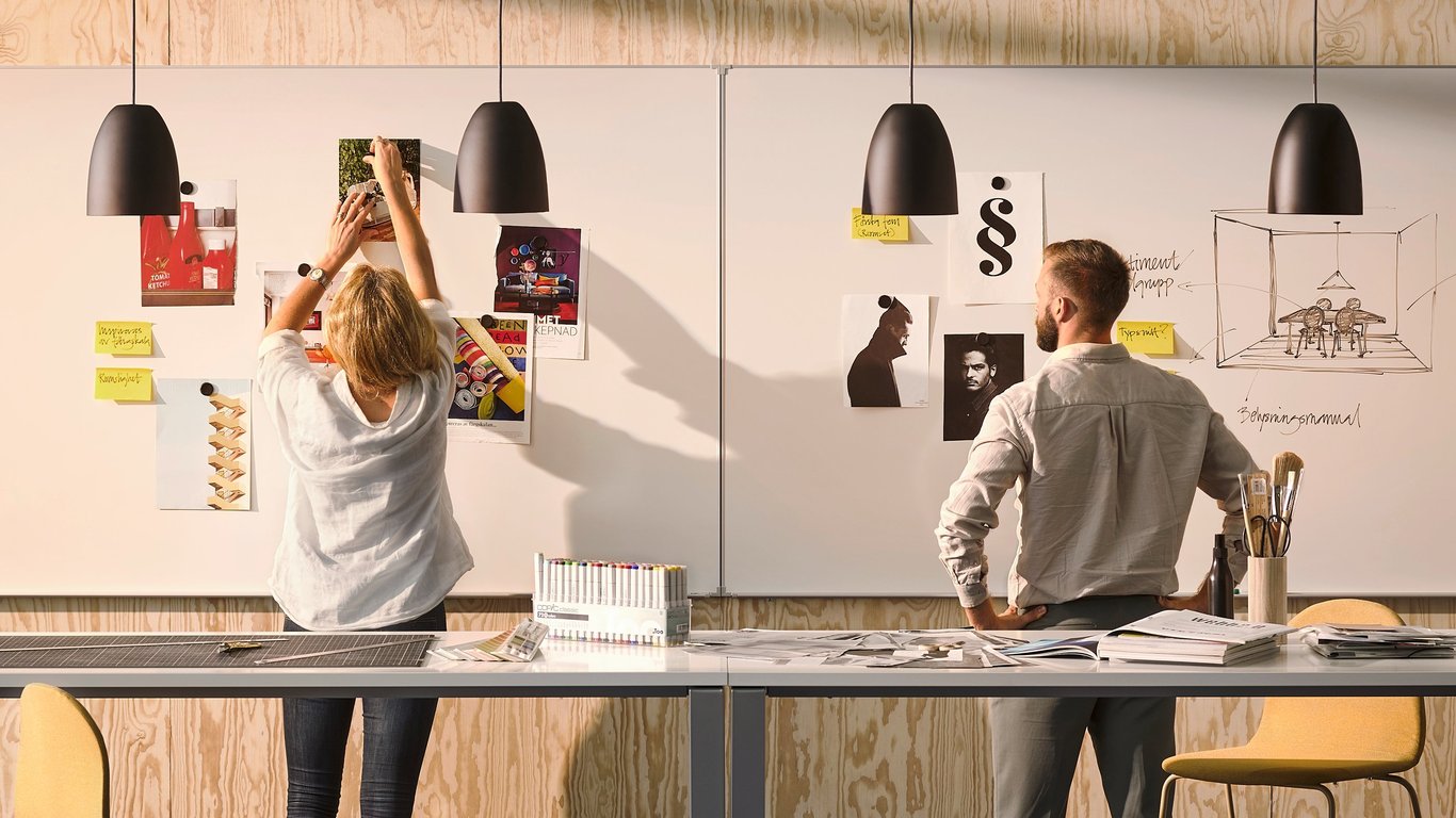 Two people standing in front of a wall-mounted whiteboard