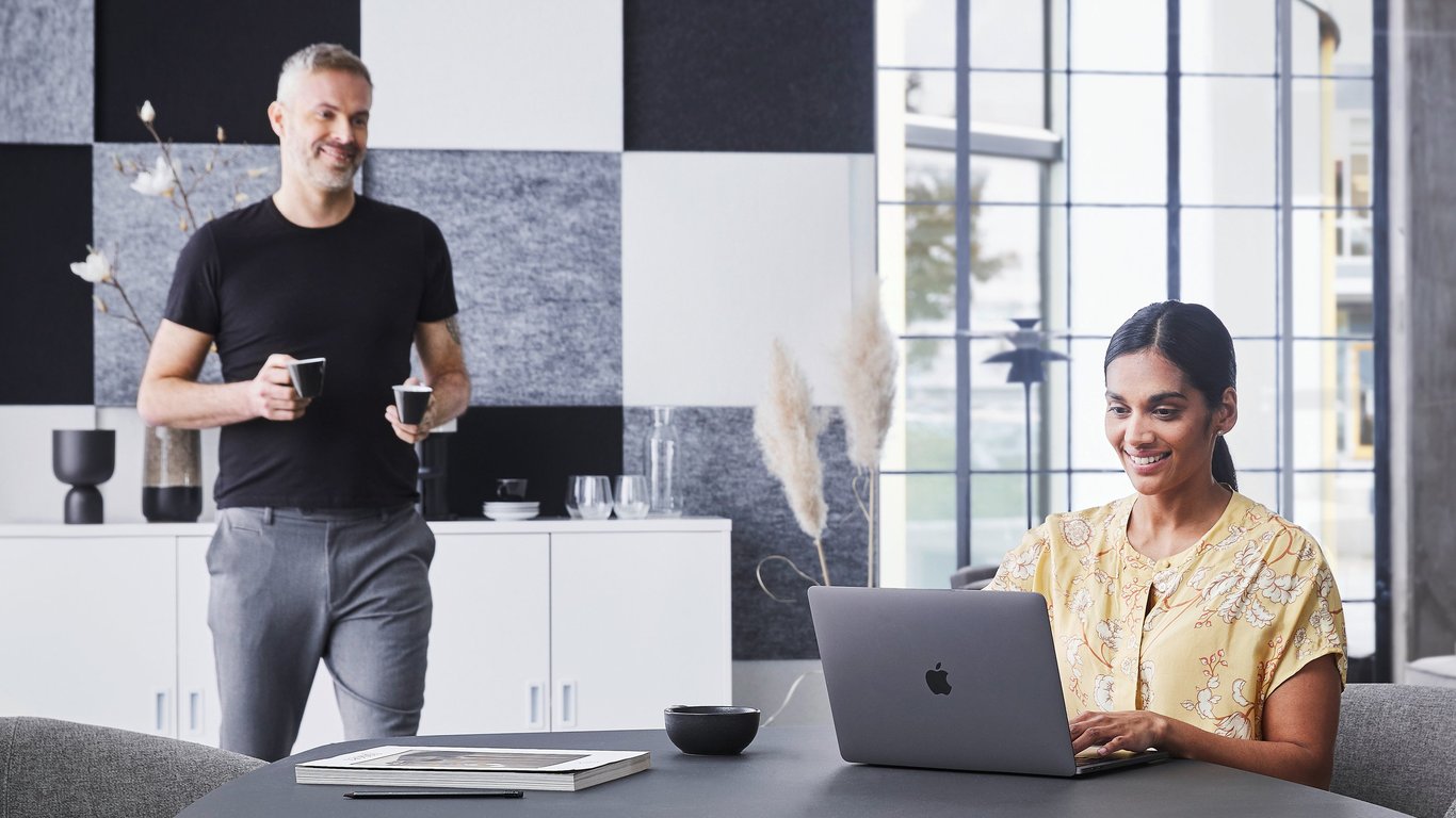 Žena radi za radnim stolom na laptopu, a muškarac donosi kavu