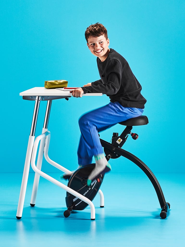 Boy sitting on a exercise bike at a desk
