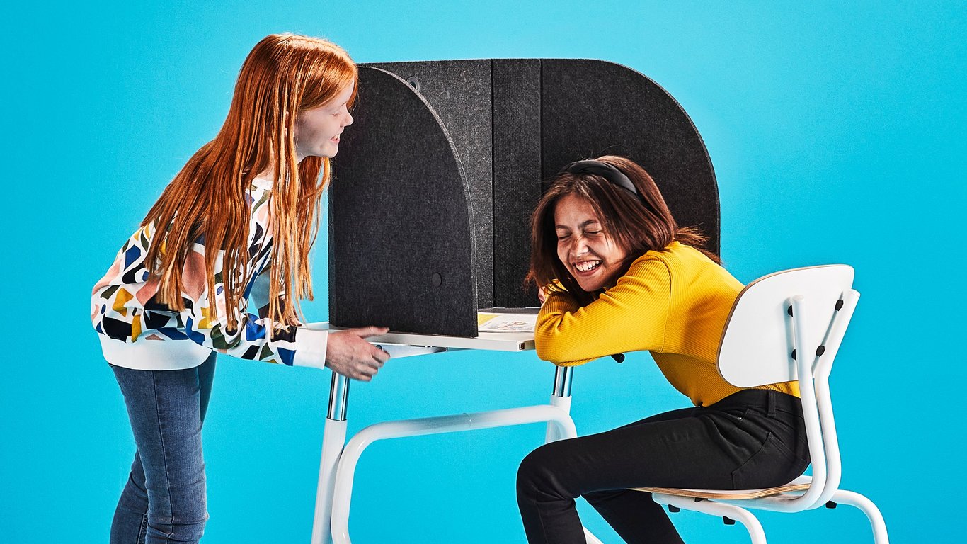 Girl sitting at a desk and laughing with another girl standing next to her