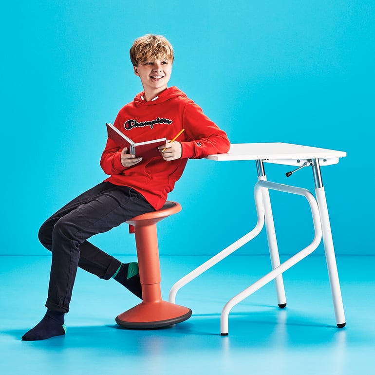 Oppilas, joka istuu aktiivituolin päällä pöytänsä äärellä