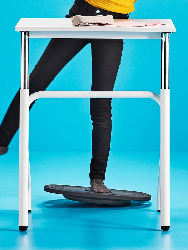 Person standing one-legges on a balance board at a desk