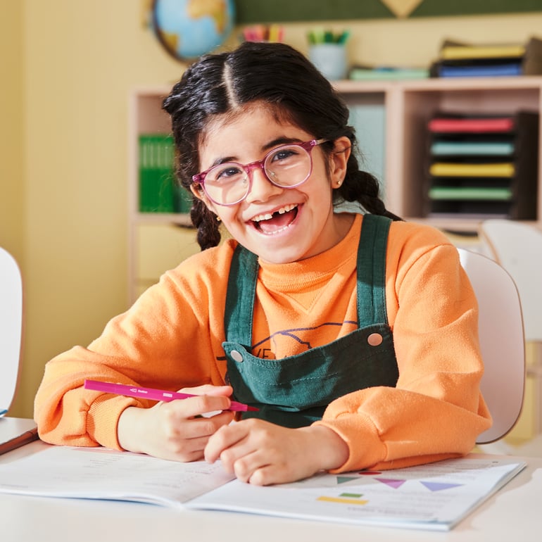 En smilende elev sidder ved et skolebord i et klasselokale