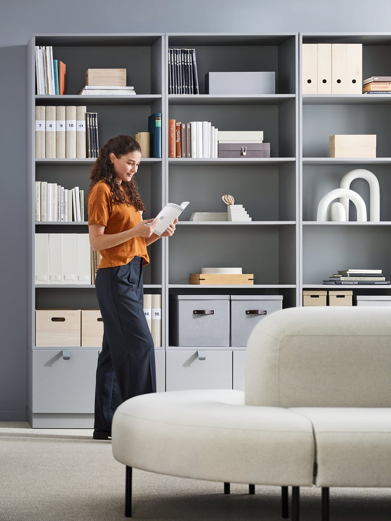 Lady reading a book stood next to bookcases and seating