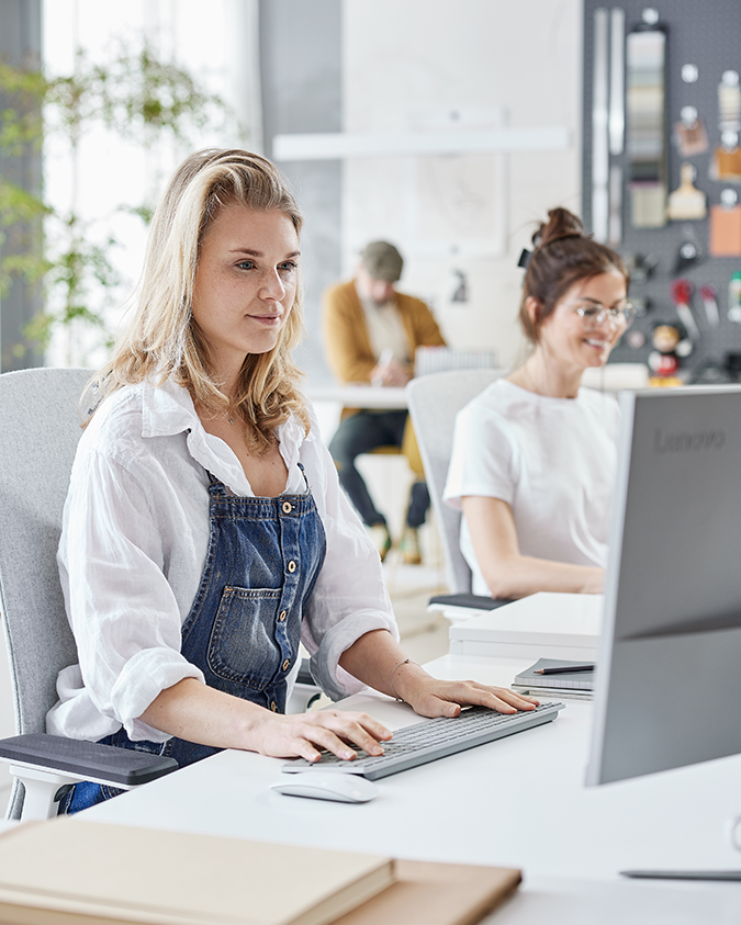 Kvinde arbejder ved computer med to kolleger i baggrunden