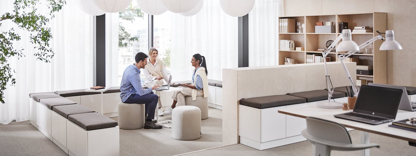 Inimesed istuvad kontoris ning vestlevad omavahel, taustaks kontoririiulid, reguleeritavad lauad, kontoritoolid ja muu kontorimööbel.
