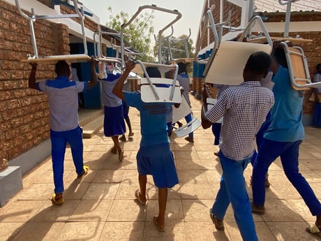 Õpilased väikeses Aafrika külas koolimööblit tassimas