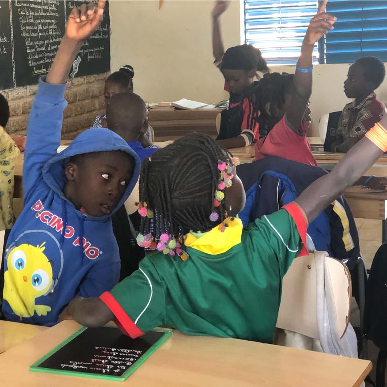 Skolebørn rækker hånden op. De sidder i deres klasseværelse i Burkina Faso, som AJ Produkter har være med til at indrette