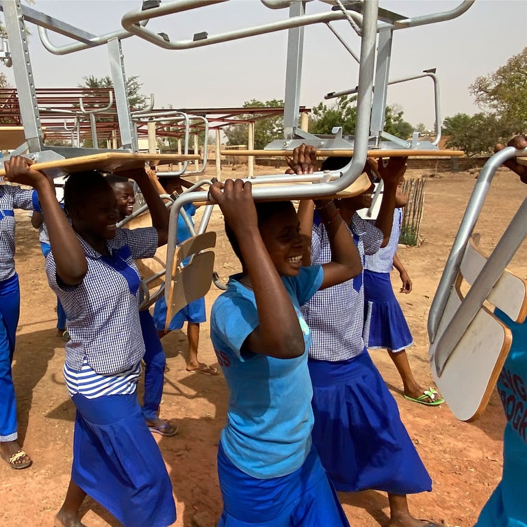 Skolebørn i Burkina Faso bærer deres skolestole fra AJ Produkter over hovedet