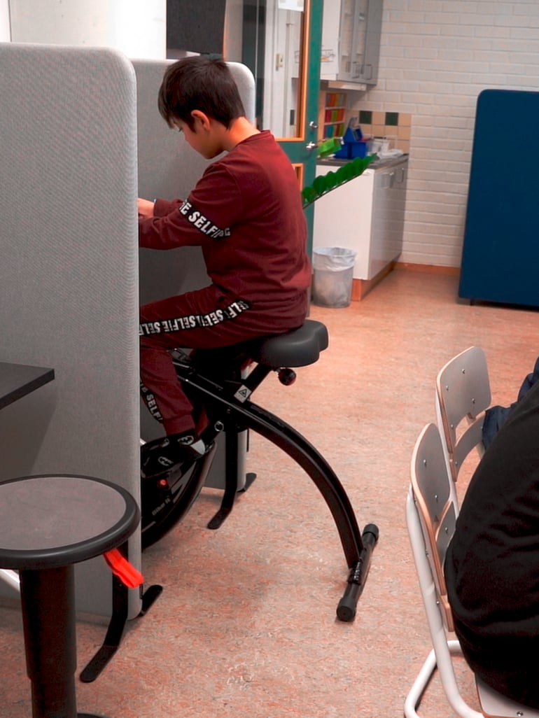 En elev fordyber sig mens han sidder på en kontorcykel, mellem to skærmvægge