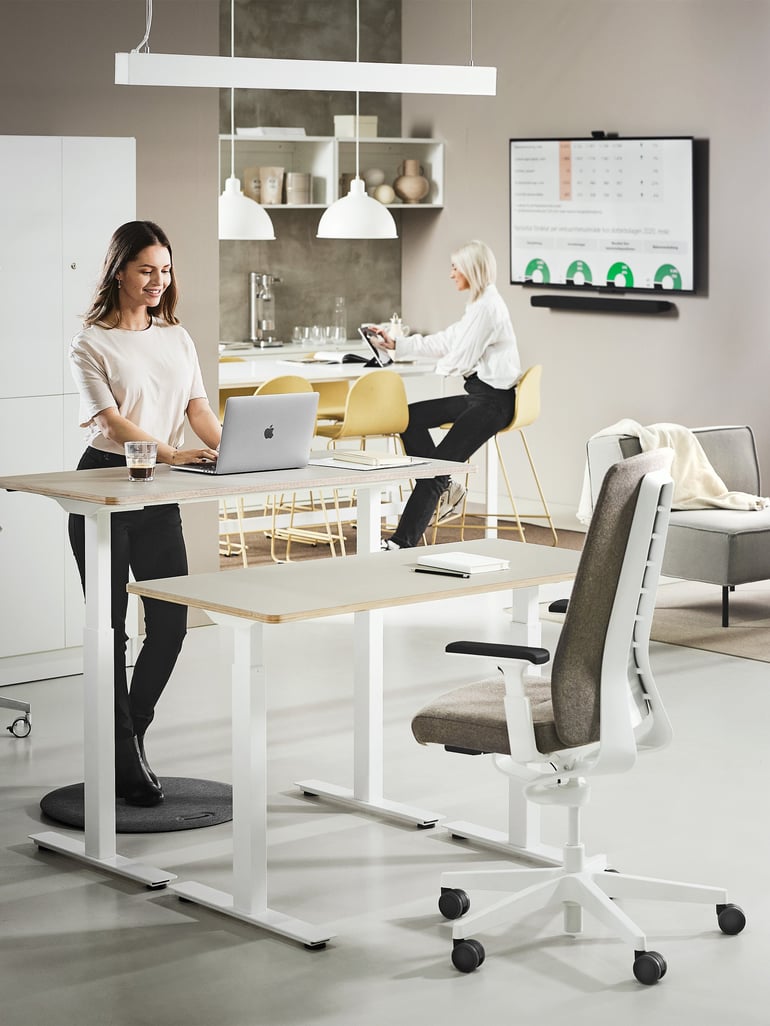 Eine Frau steht am höhenverstellbaren Schreibtisch und arbeitet