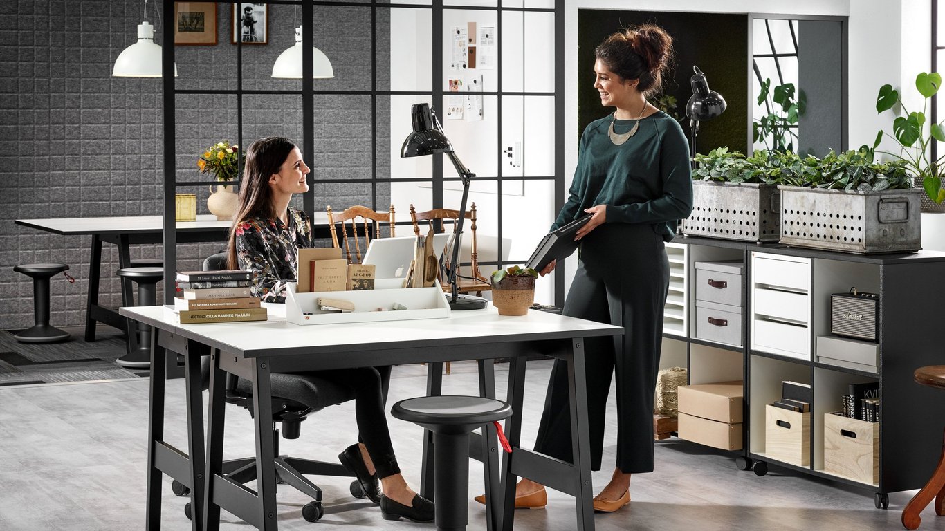 Two women, one sitting and one standing, talking in an office