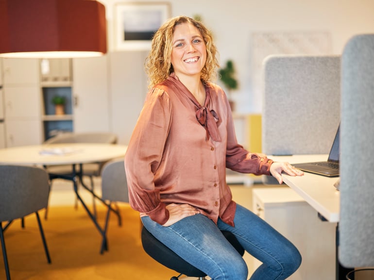 Moteris šypsosi sėdėdama prie biuro stalo