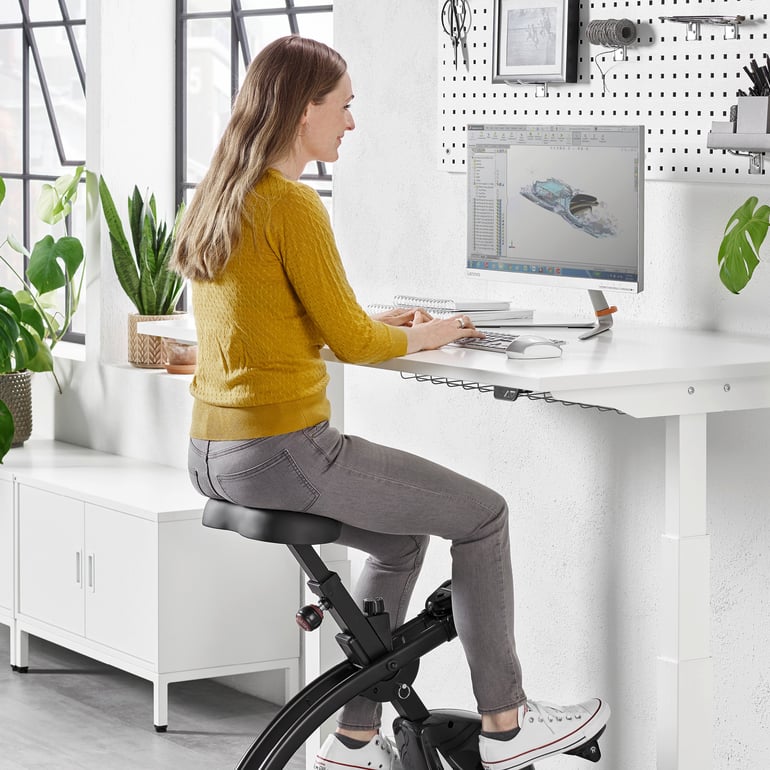 Moteris sėdi prie biuro stalo ant darbo vietos treniruoklio - dviračio