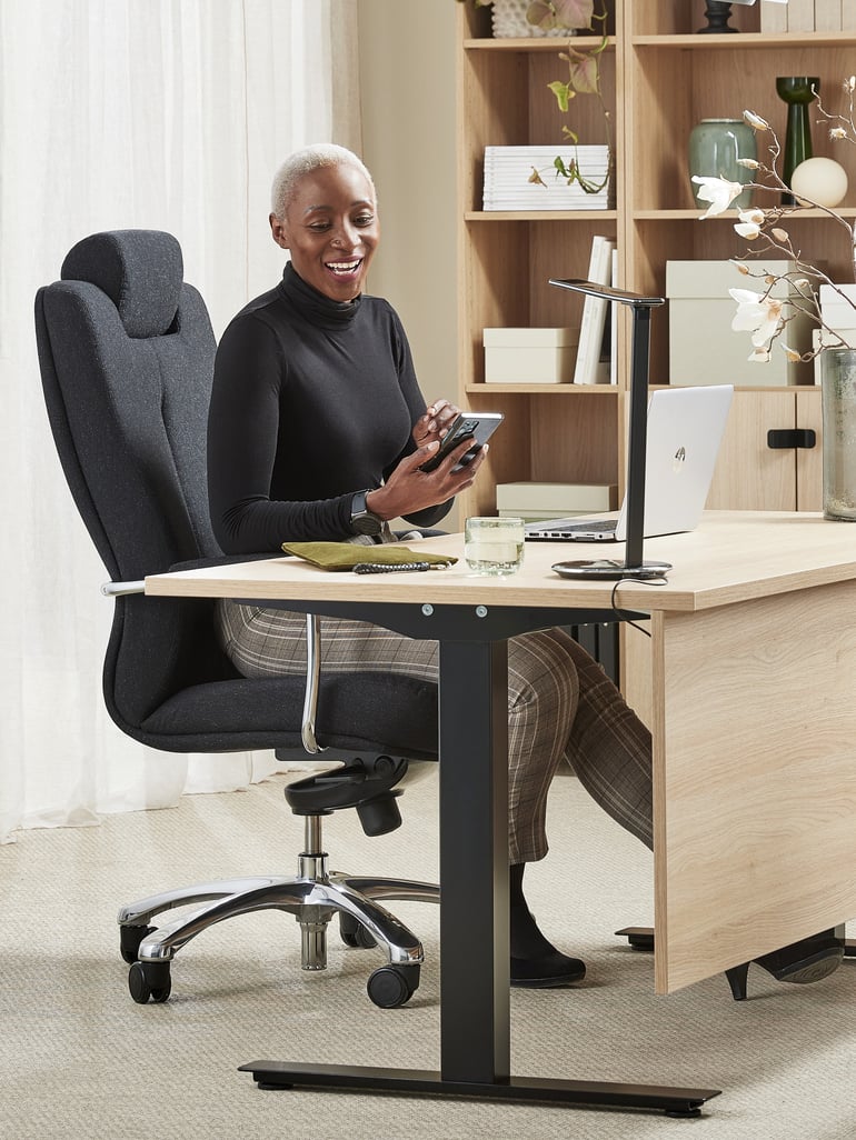 Moteris sėdi prie darbo stalo, ant biuro kėdės