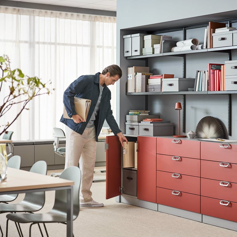 Ein Mann steht im Büro und nimmt Unterlagen raus aus einem Schrank