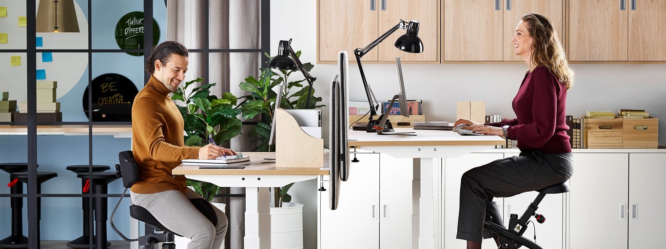 Woman sitting at desk on exercise bike and man sitting at desk on a saddle chair