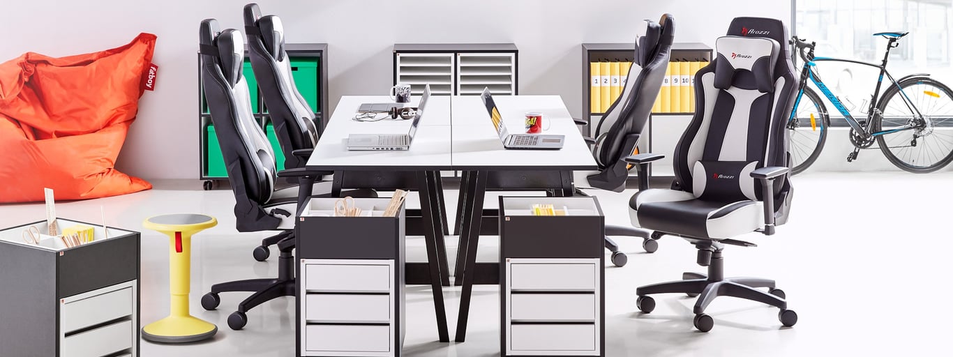 Ein ausgestatteter Raum mit Bürostühlen, Rollcontainer und Schreibtischen, die einen großen Schreibtisch bilden